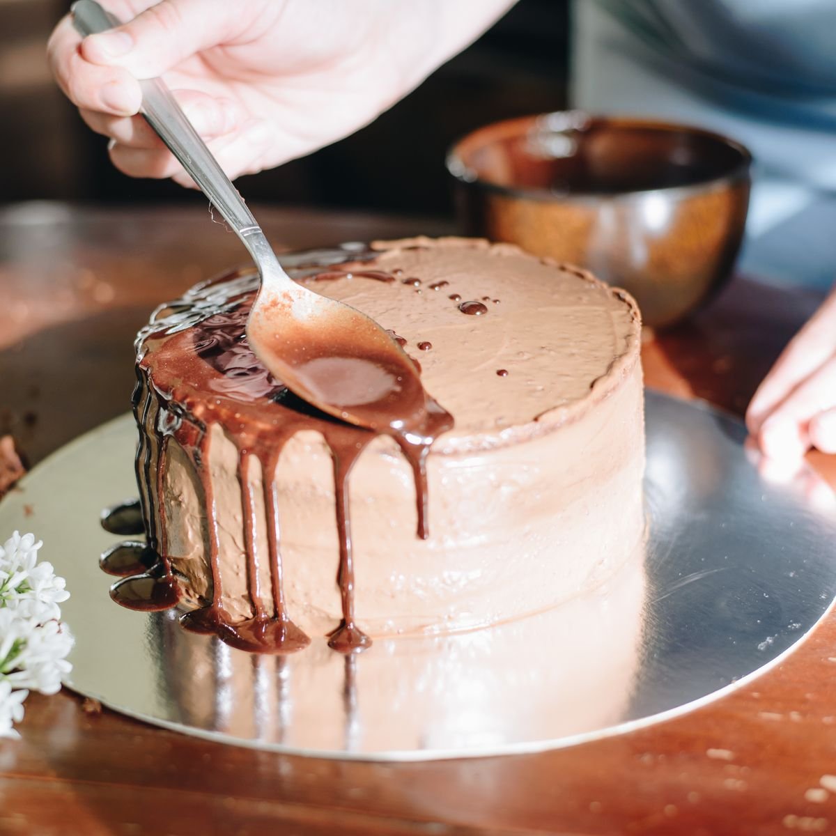 Baker finishing a chocolate drip cake on a silver Merry Boards cake board